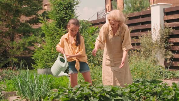 Girl With Grandmother Watering Flowers In Garden