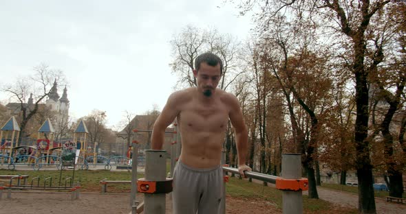 Young Man Is Doing Push Ups on Bars Outside 