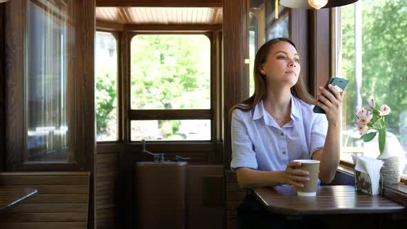 charming woman with a phone drinks coffee in a tram cafe