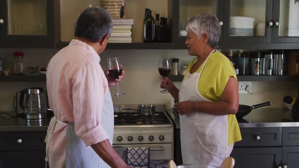 Senior mixed race couple drinking wine enjoying preparing food in kitchen