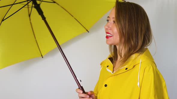 A girl in a yellow raincoat under an umbrella stretches out her hand to the rain.