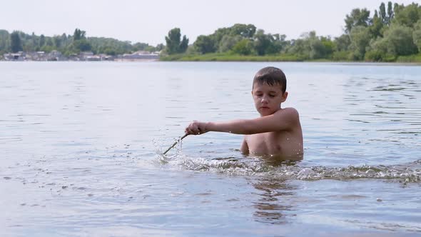 Active Child Playing with a Stick in River in Water Creating Waves Splashes