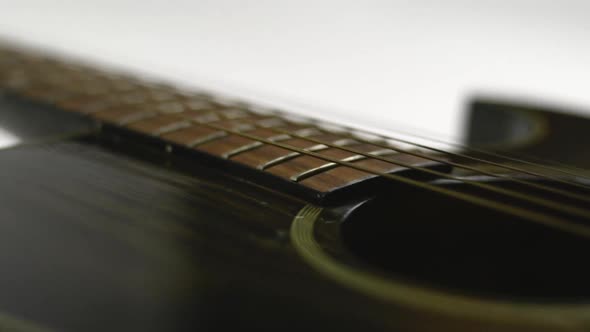 Low sideways sliding view of an acoustic guitar. From the sound hole to the head on a white backgrou