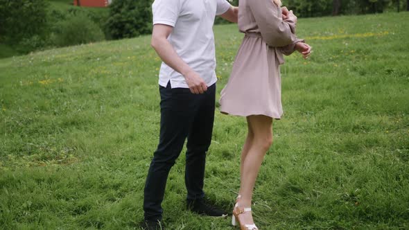 Man with a Woman Blonde in a Dress Dance on a Green Field in Nature in Summer