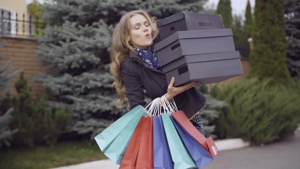 Portrait of Smiling Beautiful Young Woman Holding Heavy Shopping Boxes Walking Outdoors