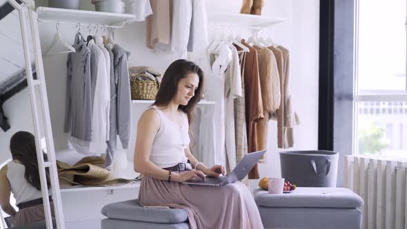 Lady Works on Laptop at Soft Pouf with Coffee and Croissant