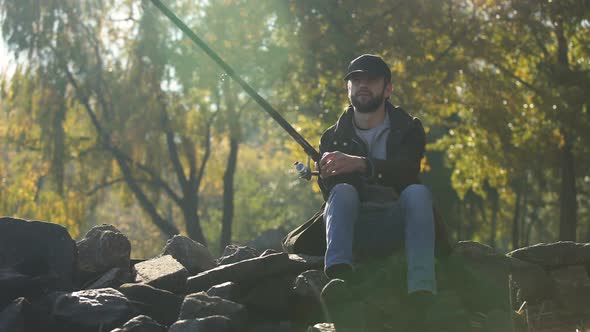 Fisherman Spinning Fishing Reel, Sitting on Stones, Enjoying Leisure, Autumn