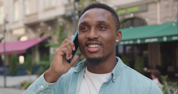 Black-Skinned Man in Trendy Clothes Has Positive Phone Conversation Nearby Cozy Street Cafe