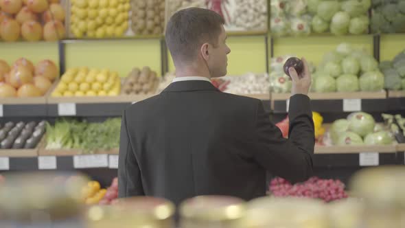 Back View of Brunette Young Caucasian Man Smelling Red Onion in Grocery. Rear View of Adult Guy in