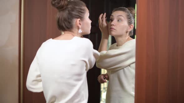 woman paints eyelashes in front of a mirror at home, going to a meeting