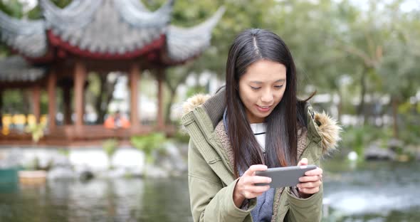 Asian Woman playing game on smart phone at china, Chinese pavilion garden
