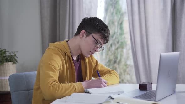 Camera Moving From Left To Right Around Young Caucasian Boy in Eyeglasses Writing and Using Laptop