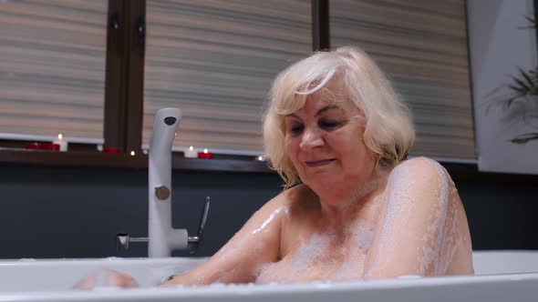 Beautiful Active Senior Woman Lying in Warm Bath with Bubbles, Enjoying Relaxation. Elderly People