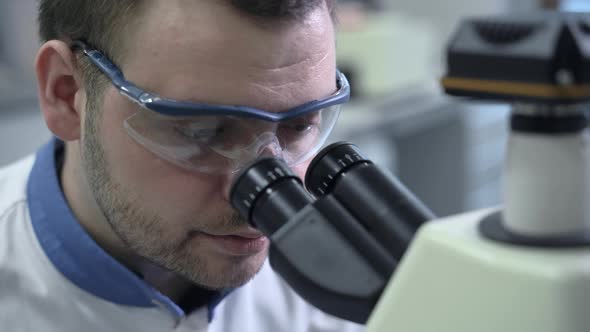 Serious Focused Male Scientist Wearing Protective Glasses Looking in Microscope Spbas