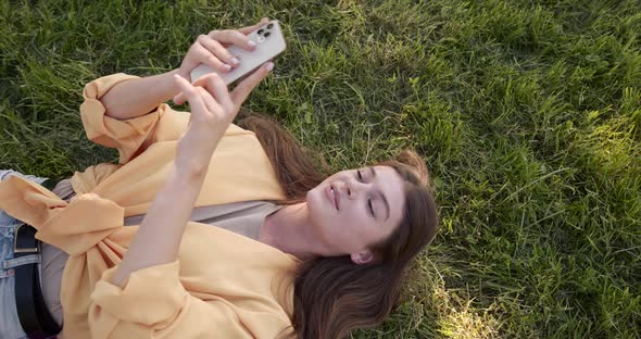 Younng Woman with Smartphone Lying on Grass