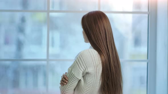 Young Woman with Long Beautiful Hair Looking on Frozen Big Window Back View