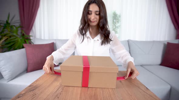 Woman closing gift box and tying it with ribbon.