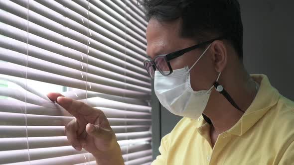 Slow-motion footage A man wearing a medical mask looks out of the window during a home quarantine.