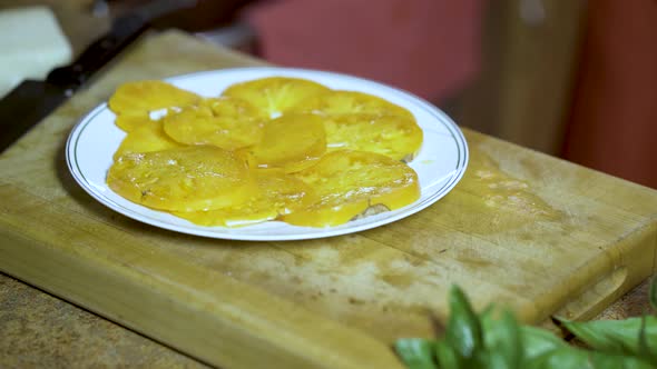 Chef takes freshly cut yellow heirloom tomato slices on a plate and sprinkles on oregano.