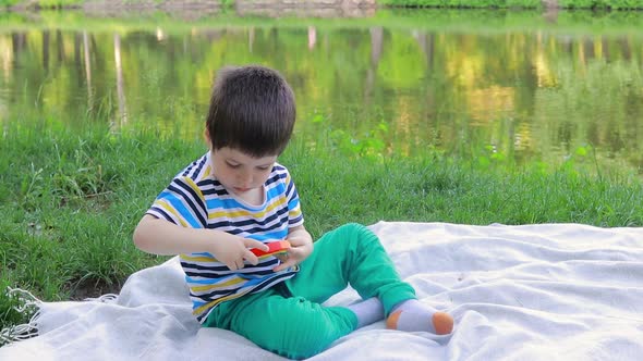 A 4 Year Old Boy Plays Pop It in Nature Near the Lake