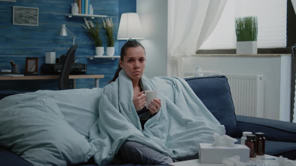 Woman with Seasonal Cold Holding Cup of Tea Wrapped in Blanket