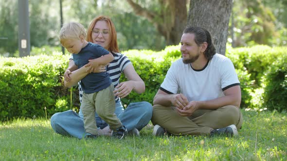 Family Spend Time in the Park  Sitting on the Grass and Mother Hugging Her Son