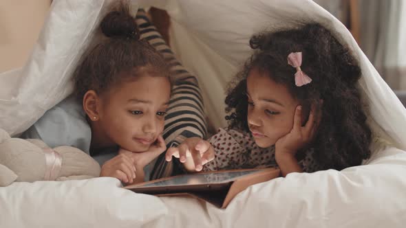 Sisters Using Tablet Computer Under Blanket