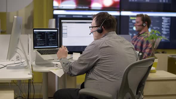 View of 2 people with headsets on in front of computers