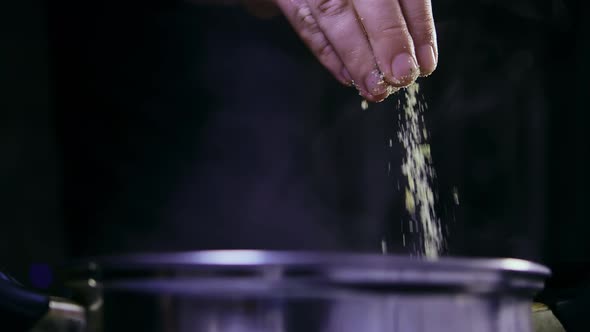 Steam from the pan, man adds spices to the pan, dark background