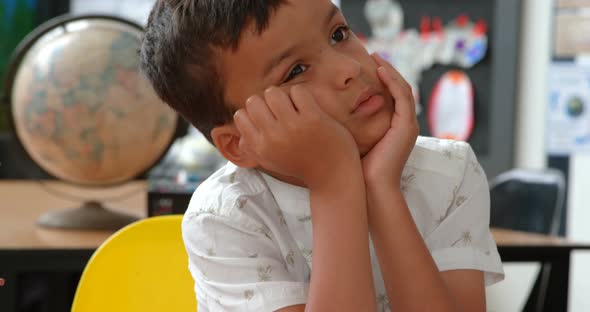 Front view of thoughtful Asian schoolboy leaning on hands at desk in classroom 4k