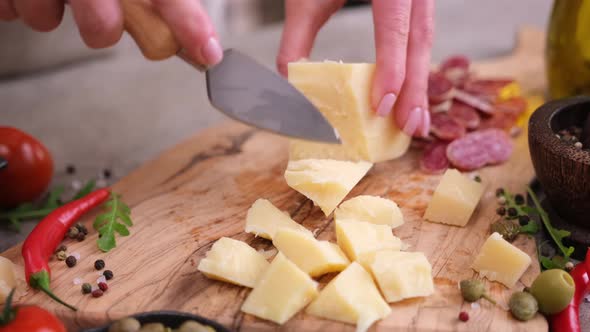 Woman Chopping Parmesan Cheese Piece with Knife on Wooden Board at Domestic Kitchen