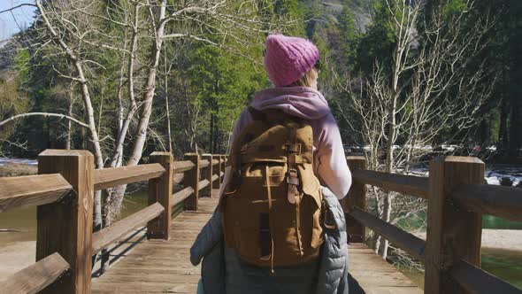 Back View of Woman Hiker By Wooden Bridge on Sunny Spring Day in Mountain Valley
