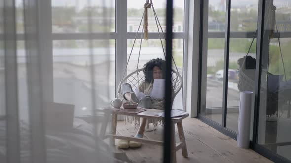 Portrait of Thoughtful Confident Woman Analyzing Business Sitting in Hanging Chair in Bedroom