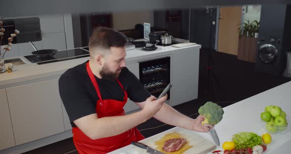 Young Man Cooking at Home and Taking Photo of Broccoli on Smartphone