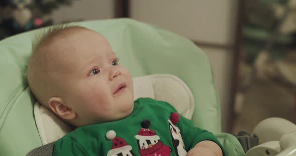 Capricious Christmas Toddler in Kid Chair During Feeding with Spoon By Mother