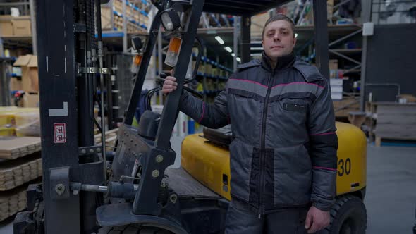 Portrait of Proud Confident Warehouse Loader in Uniform Looking at Camera Standing at Equipment in