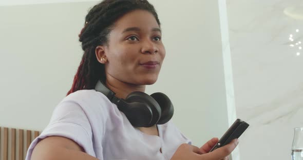 Portrait of Attractive Afro Woman with Black Headphones and Smartphone Sitting in a Cafe and Smiling