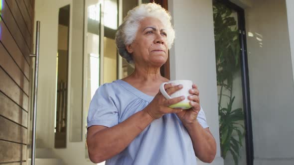 African american senior woman drinking coffee while standing at the front door at home