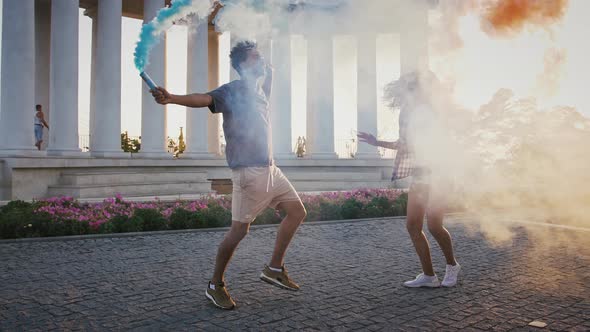 Darkskinned Pair Smiling and Waving Colorful Smoke Bombs While Dancing in Park