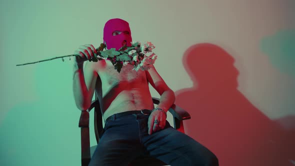 Anonymous Shirtless Man in Balaclava Sitting with Flowers