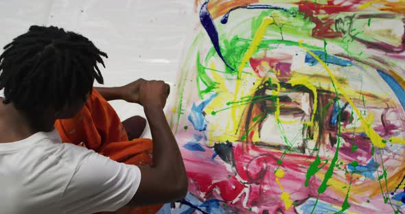 Overhead view of african american male artist pouring paint with a paint brush on canvas