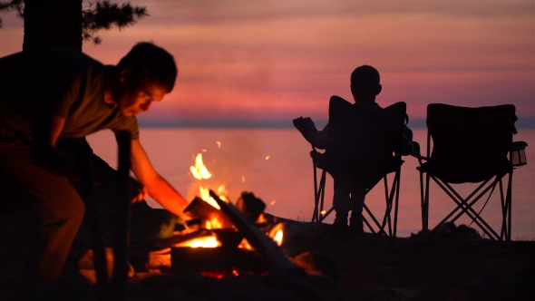 Father with Child Are Sitting Near Campfire at Night.