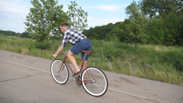 Young Handsome Man Riding at Vintage Bicycle in the Country Road. Sporty Guy Cycling at the Track