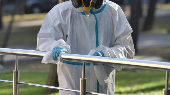 The Person of the Disinfector in a Protective Suit Sprays the Disinfectant on the Handrail and Wipes