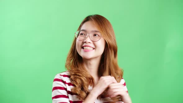 Happy playful Asian girl with eyeglasses smiling and playing with her hair over green screen.