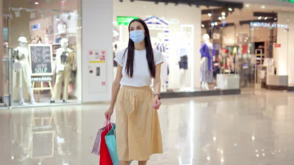 Woman in Medical Mask with Bags Walking in Shopping Center