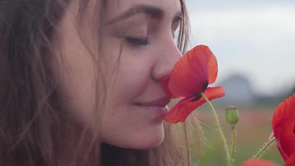 Portrait of Cute Young Woman Smelling Red Poppy Flower Standing in a Poppy Field
