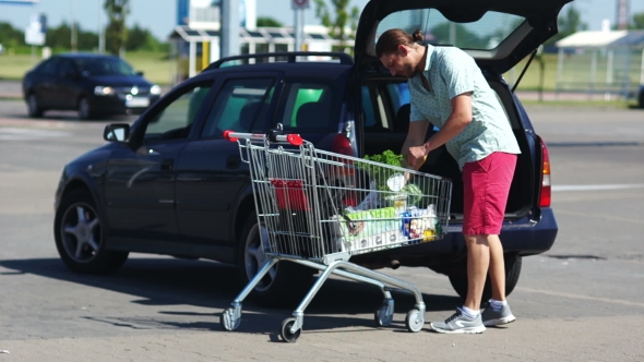 Father Loading Foods From Shopping Cart Into Car Trunk at Parking Lot