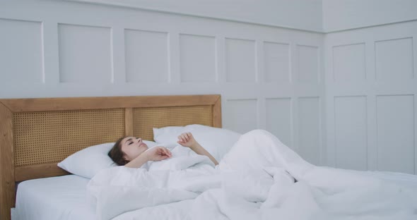 Young Woman Wakes Up in Bed in the Morning Smiling Raises Her Hands
