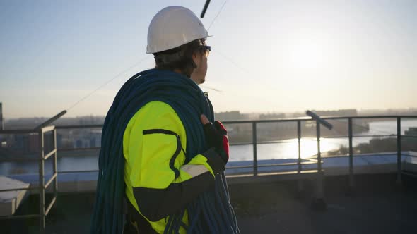 Climber with Skein of Rope on Shoulder Walks Along Rooftop